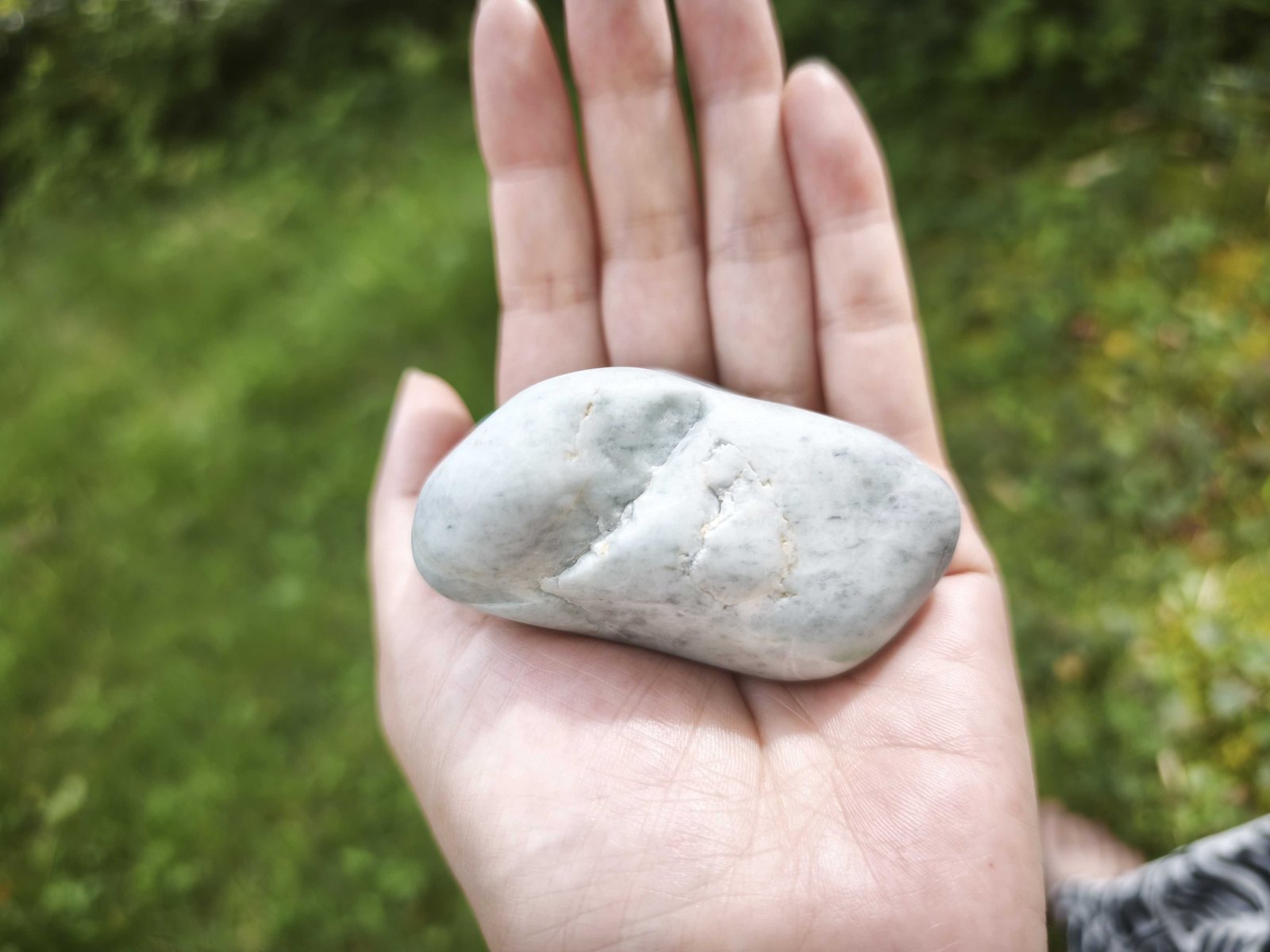 開いた手のひらに、白みがかった緑の丸い石をひとつ載せている。背景は芝生